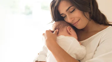 kvinne som ser tilfreds ut mens hun holder babyen sin tett inntil seg.