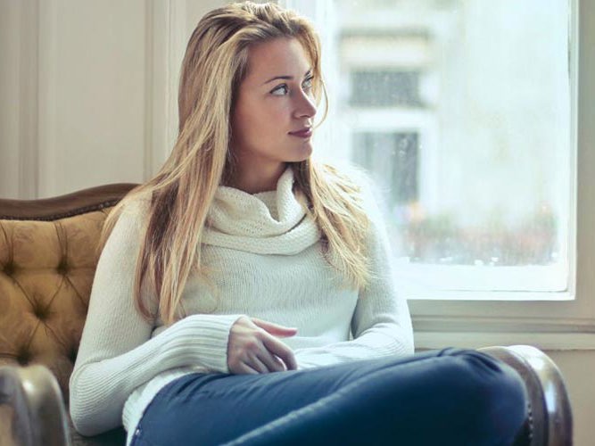 Ung kvinne som sitter og tenker på noe mens hun ser ut av et vindu.