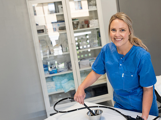 Kvinne som smiler og holder et skop inne på et behandlinsrom.