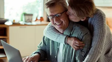 Et voksent par smiler og klemmer mens de leser noe på en PC.